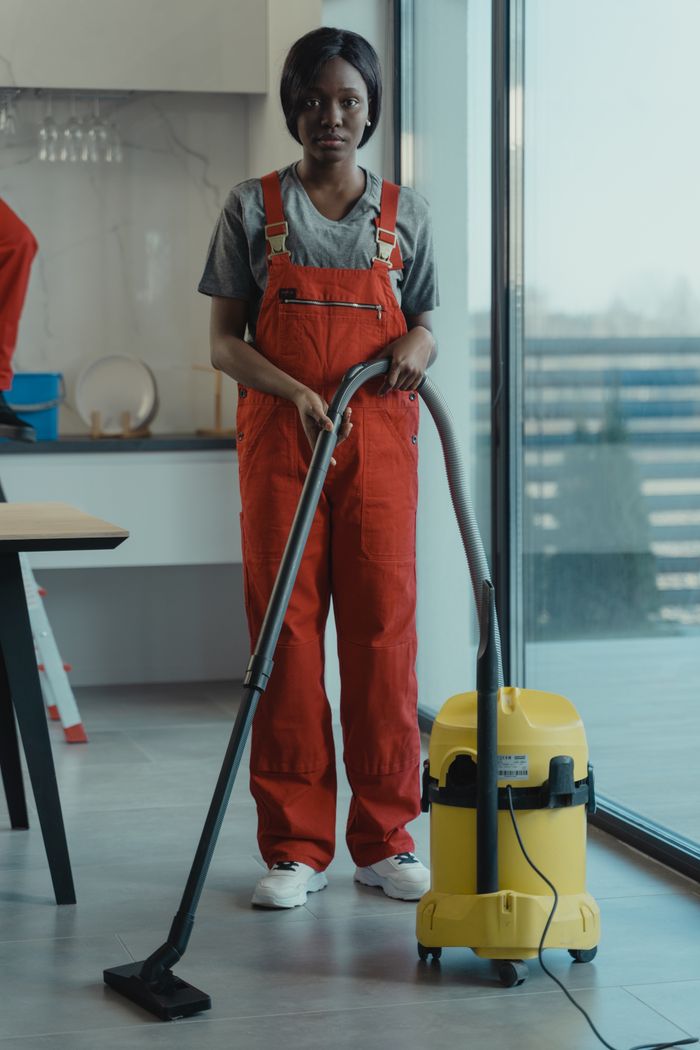heros-img An adult woman in red coveralls operates a vacuum cleaner in a modern indoor setting, focusing on cleaning tasks.